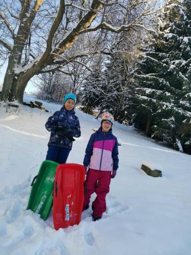 two girls are standing in the snow on a playground at Penzion Pastviny in Pastviny
