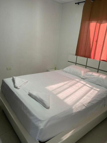 Una cama blanca con sábanas blancas y una ventana roja. en Apartamento Ucha, en Ríohacha