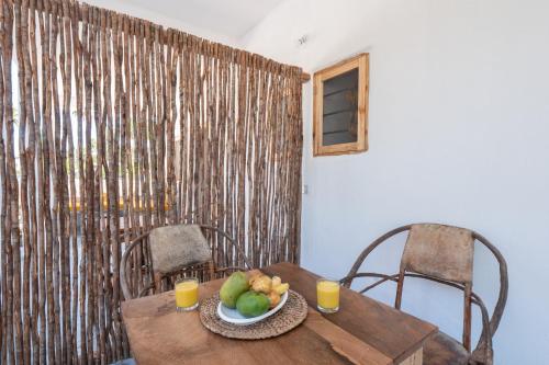a wooden table with a bowl of fruit and two glasses of orange juice at BONDENI BEACH HOUSE in Jambiani