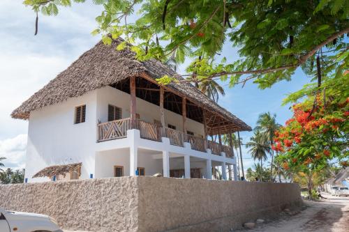 a white building with a thatched roof at BONDENI BEACH HOUSE in Jambiani