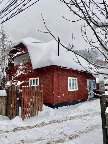 une maison rouge recouverte de neige dans l'établissement Casa Fântâna - La poalele muntilor -50 de metri de pârtia Olimpică, à Statjunea Borsa