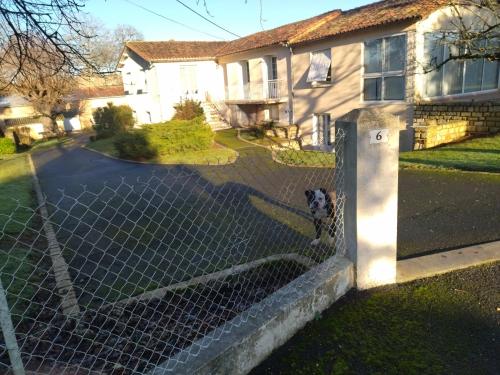 a dog standing behind a fence in front of a house at chambre privée chez l'habitant et partage des partie communes in Chail