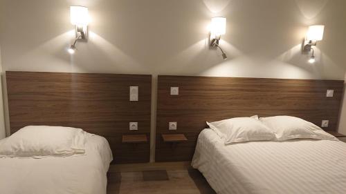 two beds in a bedroom with two lights on the wall at Hôtel de L'Europe in Gramat