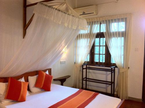 a bedroom with a bed with white curtains and a window at Little Paradise Tourist Guest House and Holiday Home in Anuradhapura