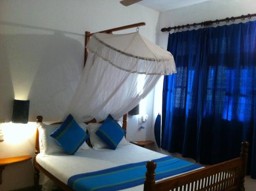 a bedroom with a bed with a canopy and blue curtains at Little Paradise Tourist Guest House and Holiday Home in Anuradhapura