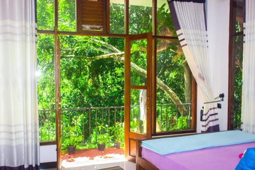 a bedroom with a large window with a tree outside at Pepper Garden Resort in Ella