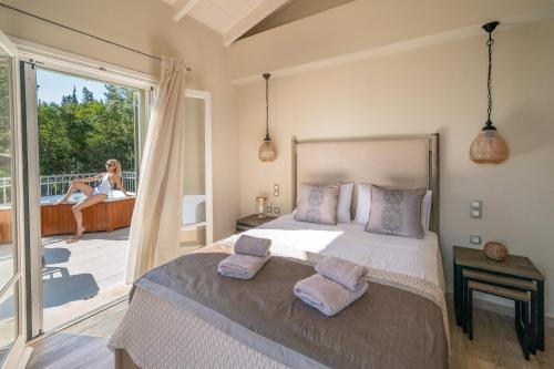 a bedroom with a bed and a woman sitting on a balcony at Luxury villa above emblisi beach , with heated pool ! in Fiskardho