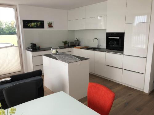 una cocina con armarios blancos y una silla roja en Schickes Ferienappartement, en Lochau