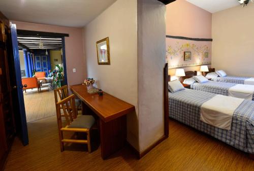 a hotel room with two beds and a desk and a table at Hotel Posada del Angel in Cuenca