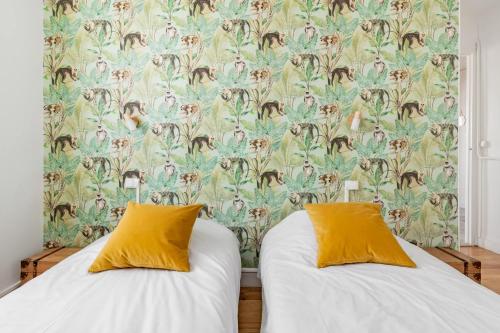 two beds with yellow pillows in a room with a wallpaper at Bel appartement avec garage sur l'île de Nantes in Nantes