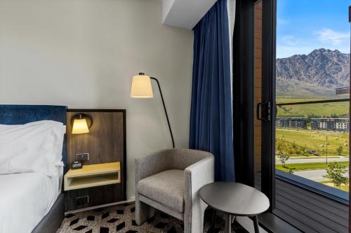 a bedroom with a bed and a chair and a window at Holiday Inn Queenstown Remarkables Park in Queenstown