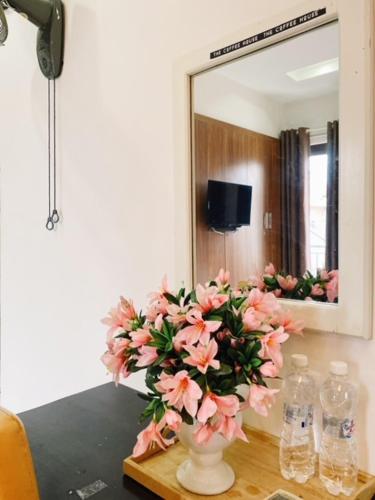 a vase with pink flowers on a table in front of a mirror at Poetic Hue Hotel & Spa in Hue