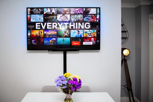 a television on a wall with a table and flowers at St Andrews Guest House in Irvine