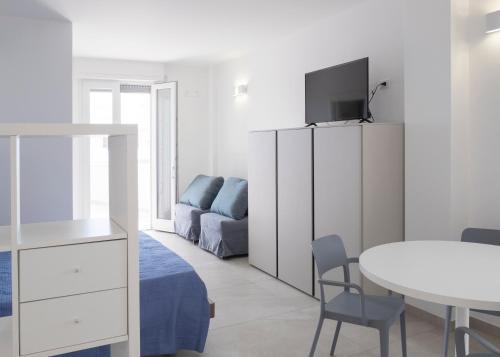 ein weißes Schlafzimmer mit einem Bett, einem Tisch und einem TV in der Unterkunft Brezza Salentina Aparthotel in Torre San Giovanni Ugento