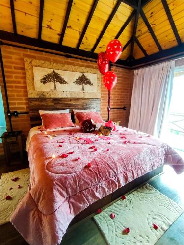 a bedroom with a bed with red pillows and balloons at Chalés Descanso na Serra in Monte Verde