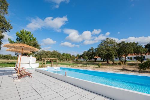 a swimming pool with an umbrella and a table and chairs at MyStay - Herdade do Vale da Abelheira in Grândola