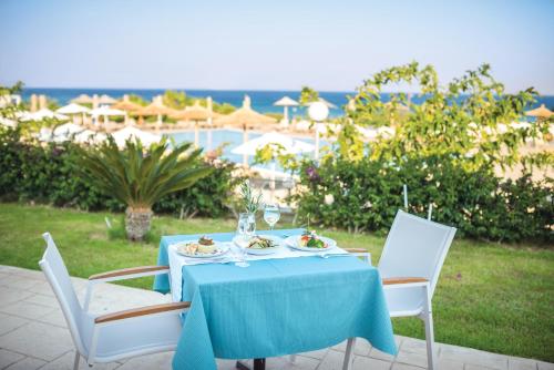 a table with a blue tablecloth and chairs and the ocean at Grand Blue Beach Hotel in Kardamaina