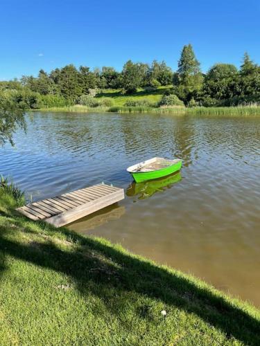 a green boat sitting next to a dock on a lake at Hyggelig sommerhus. med udsigt, til vand fra senge in Veksø
