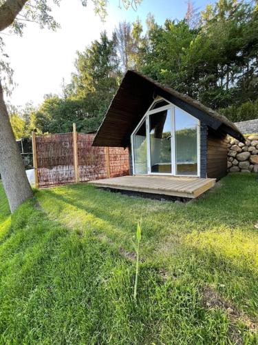 a small cabin with a large window in a yard at Hyggelig sommerhus. med udsigt, til vand fra senge in Veksø