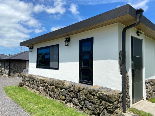 a white house with black windows and a stone wall at Jeju Time in Jeju