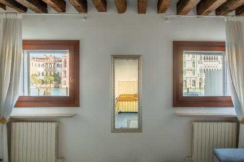 two windows with curtains and a mirror on a wall at Canaletto Apartment Rialto in Venice