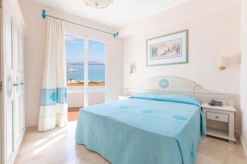 Dormitorio blanco con cama y vistas al océano en Club Hotel Cormorano, en Baja Sardinia