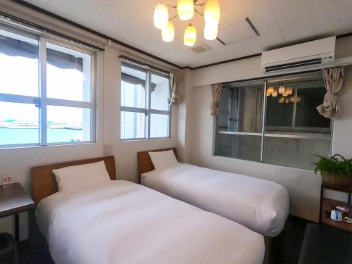 two beds sitting in a room with windows at Ishigakijima Hotel Olive in Ishigaki Island