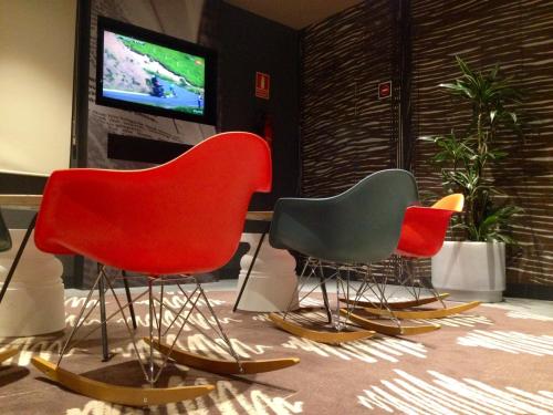 three different colored chairs in a room with a tv at Ibis Sevilla in Seville
