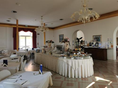 un restaurante con mesas y sillas blancas y una lámpara de araña en Hotel Lido en Rímini