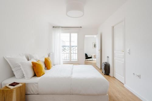 een witte slaapkamer met een groot bed met gele kussens bij Edgar Suites Levallois – Jules Verne in Levallois-Perret