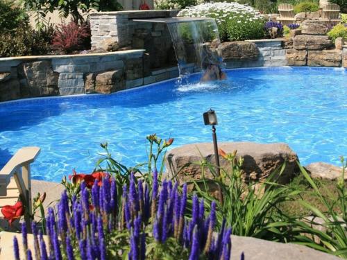 a swimming pool with a waterfall in a garden with purple flowers at Auberge Godefroy in Bécancour