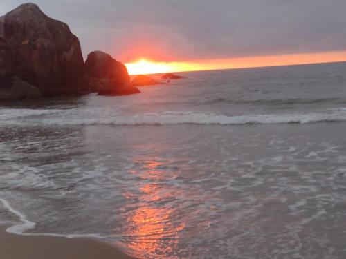 a sunset on the beach with the ocean and rocks at Sintonia do Mar in São Francisco do Sul