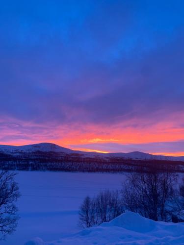 a sunset over a snow covered field with a lake at Strandgården Fjällnäs in Tänndalen