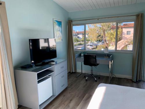 a bedroom with a television and a desk and a window at Inn at East Beach in Santa Barbara