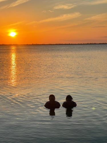 two people floating in the water at sunset at Golden Lake Apart Hotel Arraial do Cabo in Arraial do Cabo
