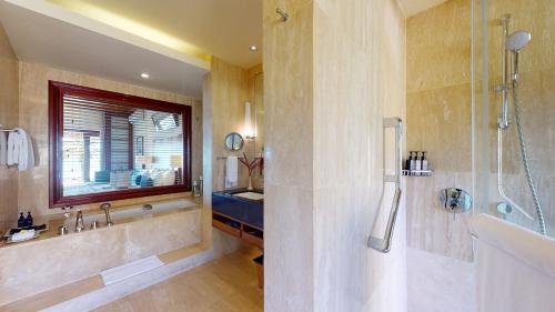a bathroom with a tub and a shower with a window at Shanti Maurice Resort & Spa in Bel Ombre