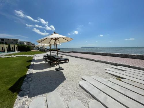 a beach with benches and an umbrella and the ocean at Residence By Hello Pattaya At Veranda in Jomtien Beach