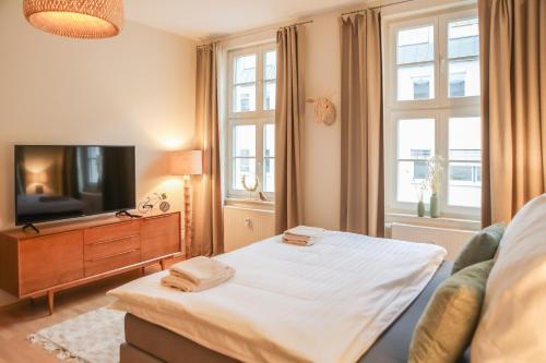 Schlafzimmer mit einem Bett, einem TV und Fenstern in der Unterkunft Sleepwell Apartment - Emilienblick in Leipzig