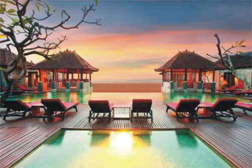a resort with chairs and a pool with a sunset at Mercure Kuta Bali in Kuta