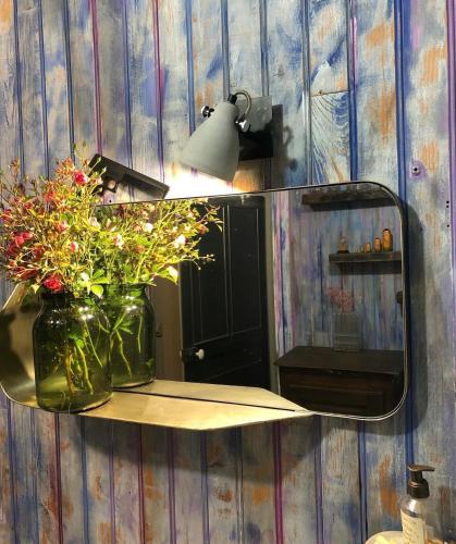 un miroir sur un mur avec un vase fleuri dans l'établissement Dealettante, à Bétaucourt