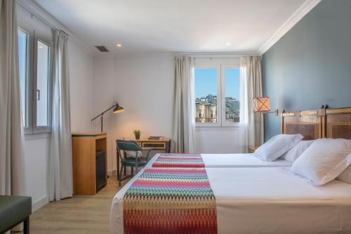 um quarto de hotel com uma cama, uma secretária e uma janela em Hotel Don Curro em Málaga