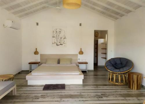 Sleeping Elephant Beach Resort في تانجالي: غرفة نوم بيضاء بسرير وكرسي