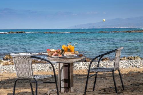 een tafel en stoelen op het strand met een drankje bij Iliostasi Beach Apartments in Chersonissos