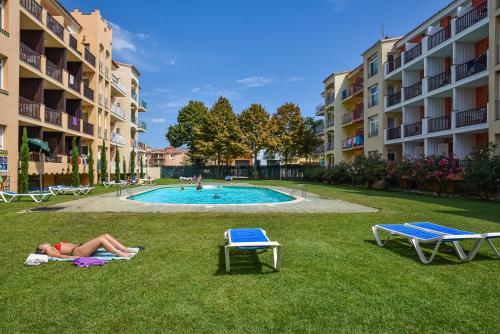a woman laying on the grass next to a swimming pool at Aptos. Comte D´Empuries in Empuriabrava