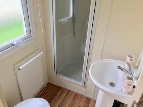 a white bathroom with a shower and a sink at Sycamore Caravan in Mullion