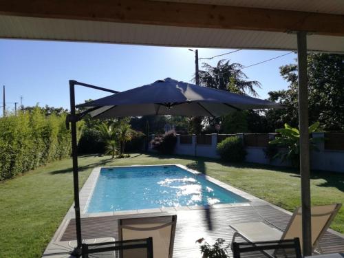 - une piscine avec un parasol et deux chaises à côté dans l'établissement VILLA LES COQUELICOTS, à Gujan-Mestras