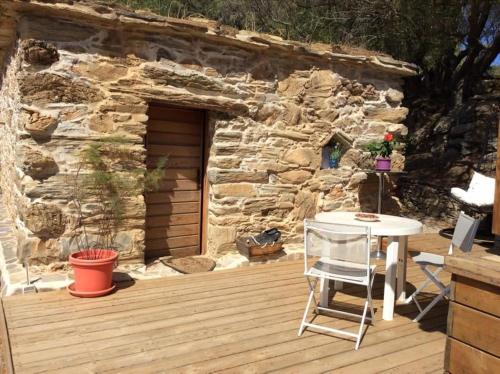 una terraza de madera con una mesa y una pared de piedra. en Bergerie tout confort L'immortelle, en Saint-Florent