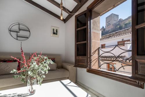 BnS Dauro Suites في غرناطة: غرفة مع نافذة و مزهرية مع الزهور على طاولة