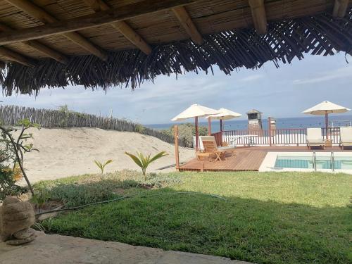 un resort con piscina e spiaggia con ombrelloni di Posada del Mar Vichayito a Los Órganos