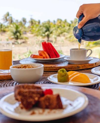 een tafel met borden met eten en een persoon die koffie inschenkt bij Pousada Paraiso dos Ventos Preá in Prea